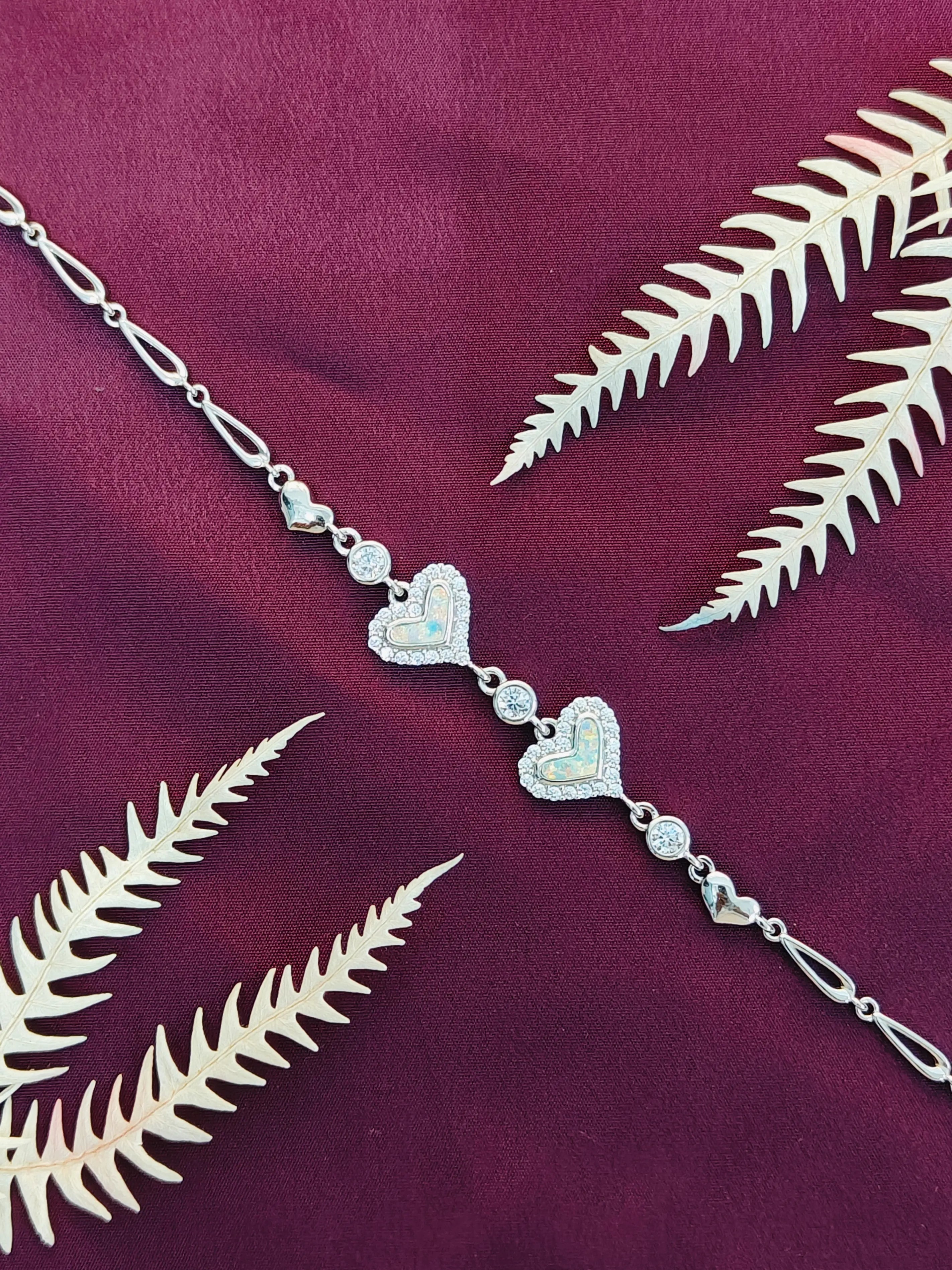 Silver heart-shaped necklace on a purple fabric background with white fern leaves